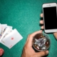 Playing cards and dice laying on casino table, with player holding glass of whiskey and mobile phone