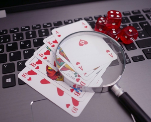 Royal flush poker cards on grey laptop with dice and magnifying glass
